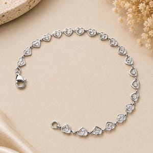 May include: A silver-toned chain bracelet featuring a series of connected heart-shaped links. Each heart link contains a textured, star-like pattern in the center. The bracelet is secured with a lobster claw clasp and a circular jump ring.