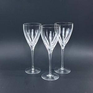 May include: Three clear glass wine glasses with a vertical etched pattern. The glasses are arranged in a row on a black surface.