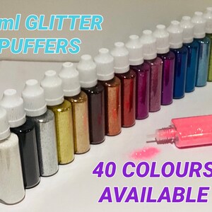 May include: A collection of 30 ml bottles of glitter, with a variety of colours, including gold, silver, black, red, pink, blue, and green. The bottles have white caps and are arranged in a row. The text "30ml GLITTER PUFFERS" is at the top of the image, and the text "40 COLOURS AVAILABLE" is at the bottom of the image.
