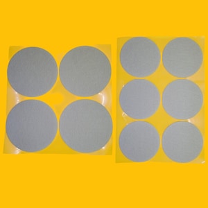 May include: Two sheets of adhesive-backed felt circles. The first sheet has four circles, the second sheet has eight circles. All circles are light grey.