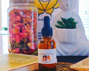 Puede incluir: Una botella de vidrio marrón con un cuentagotas, etiquetada como "A's Awesome Anti Acne & Aging Aid", está sobre una mesa. Un frasco lleno de pétalos de rosa rosados y una estatua de Buda blanca están en el fondo. También se ven un libro y un patrón geométrico decorativo.