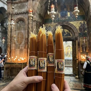 May include: Four bundles of thin, golden-yellow beeswax candles, each tied with a rubber band and featuring a rectangular paper label. The labels display an illustration of a religious figure and the text JERUSALEM and IERUSALIM in Cyrillic.