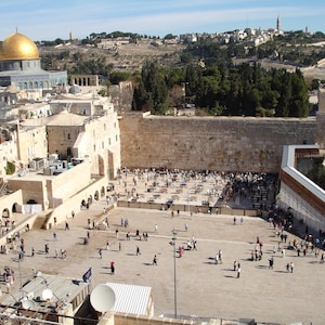 May include: An aerial view of the Western Wall in Jerusalem, Israel. The wall is made of large, rough-hewn stones and is surrounded by a plaza where people are praying. In the background, the Dome of the Rock, a golden-domed mosque, can be seen.
