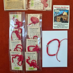 May include: A collection of red string bracelets packaged with prayer cards titled The Ben Porat Prayer and Prayer for Traveler, alongside a Kabbalah Red Strings against evil eye card and a single red string bracelet with a silver hamsa charm.