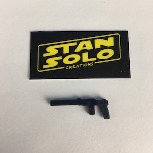 May include: A black plastic toy blaster gun with a textured grip. The gun is made by Stan Solo Creations.