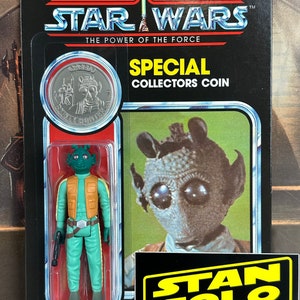 May include: A vintage Star Wars action figure of a green alien with a brown vest and a blaster pistol. The figure is packaged in a plastic blister pack with a silver collector's coin and a Stan Solo Creations sticker.