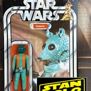 May include: A vintage Star Wars action figure card featuring Greedo, a green alien with a brown vest and a blaster pistol. The card has a black background with white text and a picture of Greedo from the movie. The card also has a sticker on the bottom right corner that says "Stan Solo Creations".