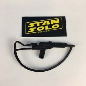 May include: Black plastic toy blaster with a curved handle. The blaster has a black grip and a black barrel. The toy is labeled "STAN SOLO CREATIONS".