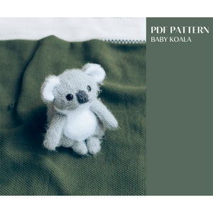 May include: A gray and white knitted koala bear toy sitting on a green blanket. The text "PDF PATTERN BABY KOALA" is in the upper right corner of the image.