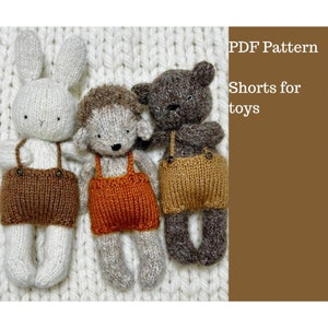 May include: Three knitted toy animals: a white rabbit, a grey hedgehog, and a brown bear, all wearing knitted shorts with braces. The shorts are in shades of brown and orange. The text "PDF Pattern Shorts for toys" is on the right.
