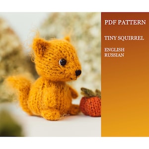 May include: A knitted orange squirrel toy with black eyes and a small, brown tail. The toy is sitting on a white surface next to a red knitted strawberry. The image includes the text "PDF PATTERN TINY SQUIRREL ENGLISH RUSSIAN".