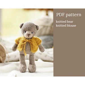 Könnte beinhalten: Ein gestrickter grauer Bär, der eine gestrickte gelbe Bluse trägt. Der Bär steht auf einer weißen Oberfläche. PDF-Muster für gestrickten Bären und gestrickte Bluse.