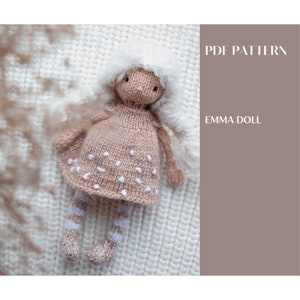 May include: A knitted doll with white yarn hair, wearing a light brown dress with white polka dots and white striped socks. The doll is lying on a white knitted surface. The text "PDF PATTERN" and "EMMA DOLL" is visible in the background.
