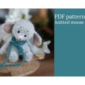 May include: A grey knitted mouse toy with teal ribbon. The toy is sitting on a woven mat. The text "PDF pattern knitted mouse" is in the background.