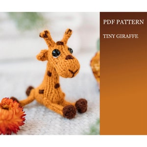 Peut inclure: Un jouet en peluche girafe tricoté avec des taches brunes et des yeux noirs. La girafe est assise sur une surface brun clair. Le texte "PDF PATTERN TINY GIRAFFE" est dans le coin supérieur droit de l'image.