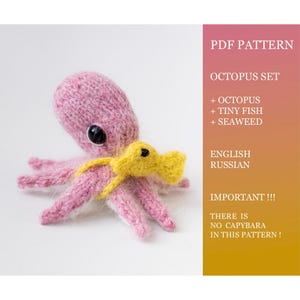 Könnte beinhalten: Ein handgefertigter, rosa gestrickter Oktopus mit einem gelben Fisch. Der Oktopus hat schwarze Augen. Das Bild enthält Text: "PDF Pattern Octopus Set + Octopus + Tiny Fish + Seaweed English Russian Important!!! There is no capybara in this pattern!"
