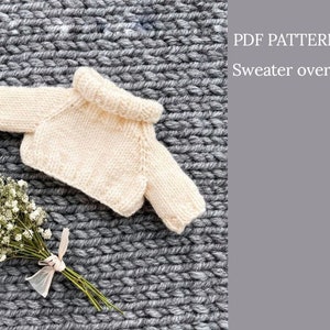 Könnte beinhalten: Ein PDF-Muster für einen gestrickten Oversize-Pullover. Der Pullover ist cremefarben und liegt auf einer grauen Strickoberfläche.