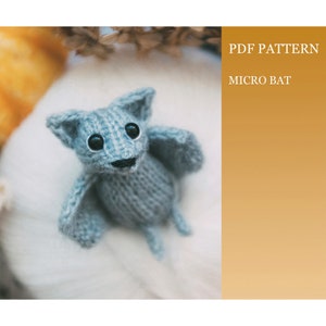 Può includere: Un piccolo giocattolo di pipistrello di maglia grigia con occhi neri. PDF PATTERN MICRO BAT.