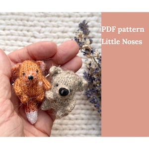 May include: Two small knitted animal toys, a fox and a bear, are held in a hand. The fox is orange and white, and the bear is brown. The text "PDF pattern Little Noses" is visible in the background.