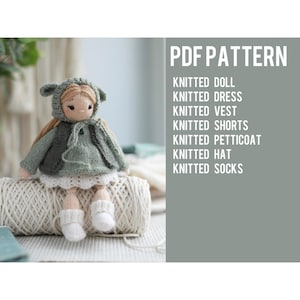 Può includere: Una bambola lavorata a maglia con un cappuccio verde salvia, un gilet verde scuro, un maglione verde chiaro, una sottogonna bianca e calzini bianchi. Il testo recita: PDF PATTERN, KNITTED DOLL, KNITTED DRESS, KNITTED VEST, KNITTED SHORTS, KNITTED PETTICOAT, KNITTED HAT, KNITTED SOCKS.