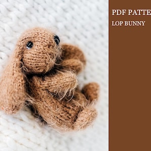 Puede incluir: Un juguete de conejo lop de punto marrón con ojos negros. El juguete está sobre una superficie de punto blanco. PDF PATTERN LOP BUNNY.