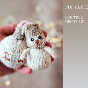 May include: Two hand-knitted Christmas ornaments. One is a snowman with a brown hat and orange nose, the other is a round ornament with brown stitching. The ornaments are made of off-white yarn. The text on the right says "PDF PATTERN FUR TREE DECOR SET".