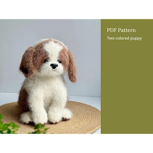 May include: A fuzzy, knitted puppy figurine with white and brown fur, featuring floppy ears, a black nose, and dark eyes. The text on the right side of the image reads: PDF Pattern, Two-colored puppy. The puppy is sitting in a seated position.