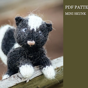 Op de afbeelding: Een zwart-wit gebreid stinkdier speelgoed met een witte streep over zijn rug. Het speelgoed zit op een houten oppervlak. PDF PATTERN MINI SKUNK.