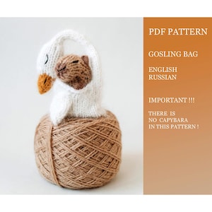 May include: A knitted white swan-shaped bag with a brown animal inside, sitting atop a ball of brown yarn. The bag has a yellow beak and black eyes. Text on the right side reads "PDF PATTERN", "GOSLING BAG", and "THERE IS NO CAPYBARA IN THIS PATTERN!"