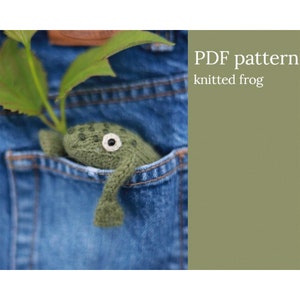 May include: A green knitted frog peeking out of a blue jean pocket. The text "PDF pattern knitted frog" is on a green background.