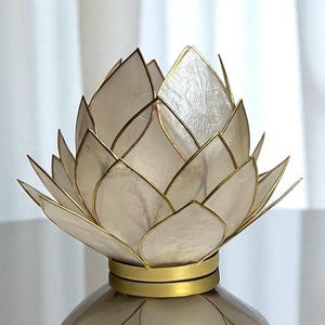 May include: A decorative lotus flower ornament with a pearlescent finish and gold-coloured trim. The layered petals create a detailed floral design. The base is also gold-coloured, and the object is set against a white background.