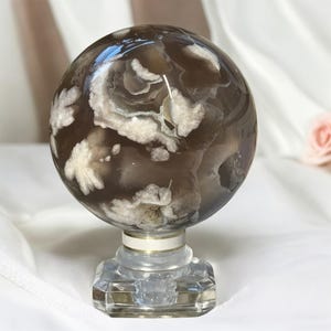 May include: A brown and white agate sphere on a clear glass stand. The sphere has a swirling pattern of white and brown.