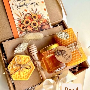 May include: A gift box containing a Happy Thanksgiving card with sunflowers, a yellow honeycomb-patterned candle, a glass jar of honey with a bee charm tag, a wooden honey dipper, and a yellow honeycomb-shaped wax piece with dried flowers.