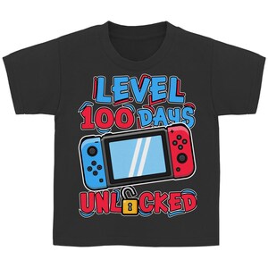 Könnte beinhalten: Schwarzes T-Shirt mit einem Videospielkonsolen-Motiv. Der Text "LEVEL 100 DAYS UNLOCKED" ist in Blau und Rot gehalten. Das Motiv zeigt ein blaues und rotes Controller-Design mit einem Bildschirm. Ein goldenes Schloss ist ebenfalls vorhanden.