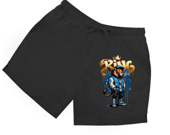 May include: Black swim shorts featuring a gold and blue graphic of a lion wearing a crown and a blue jacket. The word "King" is written in gold graffiti style. The shorts have a drawstring waist.