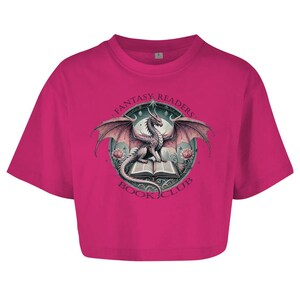 Könnte beinhalten: Ein pinkfarbenes, bauchfreies T-Shirt mit einem Aufdruck eines Drachen, der ein Buch liest. Der Aufdruck ist von einem Kreis mit dem Text "Fantasy Readers Book Club" umgeben.