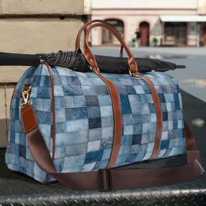 May include: A blue denim duffel bag with brown leather accents and a matching shoulder strap. The bag features a patchwork design and a black umbrella rests on top. The bag has brown leather handles and gold-colored hardware.