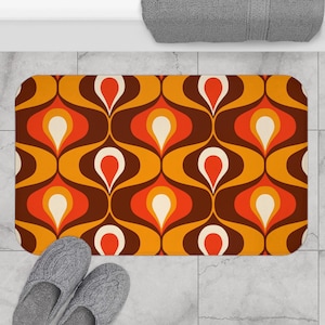 Puede incluir: Una alfombra de baño marrón, naranja y blanca con un patrón geométrico retro. El patrón presenta formas de lágrima que se repiten.