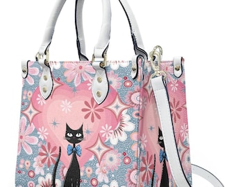 May include: A square handbag with a floral pattern in pink, blue, and white. The bag features a black cat with a blue bow tie. It has white handles and a white shoulder strap. The bag is designed with a retro, vintage aesthetic.