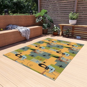 May include: A colorful outdoor rug with a repeating pattern of black cats in mid-air, with a retro starburst design. The rug is on a wooden deck.