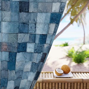 Puede incluir: Una cortina azul de retazos parcialmente retirada para revelar una vista de una playa tropical con dos mitades de coco en un plato blanco.