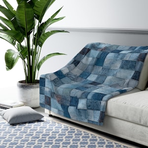 Puede incluir: Una manta de tiro de patchwork azul y blanco hecha de tela vaquera. La manta está drapeada sobre un sofá blanco con una planta verde en una maceta en primer plano.