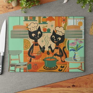 Puede incluir: Tabla de cortar rectangular con una escena de cocina retro. Dos gatos negros, chefs, con gorros blancos y delantales naranjas. Uno bate en un cuenco, el otro revuelve una olla. El fondo incluye una ventana, flores y elementos de decoración de cocina.
