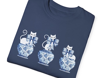 May include: Three white cats with blue bows are sitting on top of blue and white porcelain vases. The cats are all facing forward and have their tails curled around the vases. The vases are decorated with floral patterns.
