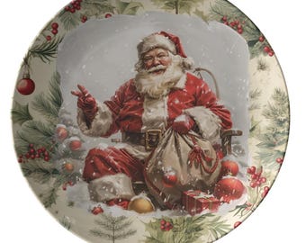 May include: A round decorative plate featuring Santa Claus in a snowy scene. Santa is wearing a red suit and hat, holding a sack of toys. The plate has a festive border with pine branches, red berries, and ornaments.