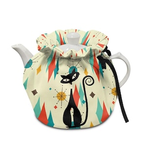 May include: A white ceramic teapot with a cream-colored cozy featuring a black cat design. The cozy has a retro pattern of red, teal, and yellow diamonds and starbursts. A black ribbon ties the cozy. The teapot has a white lid and handle.