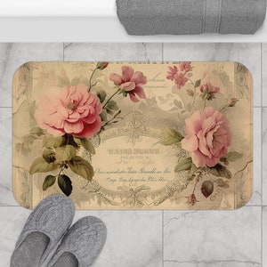May include: A vintage-style bath mat with a floral design featuring pink roses and green leaves. The mat has a beige background with a decorative border and text that reads "WARD SUITE" and "D'une collection de fleurs rares."