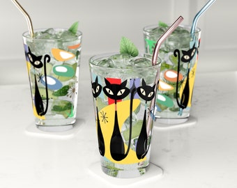 May include: Three clear glass tumblers with black cats and colorful abstract designs. Each glass has a straw and is filled with ice and a clear liquid.
