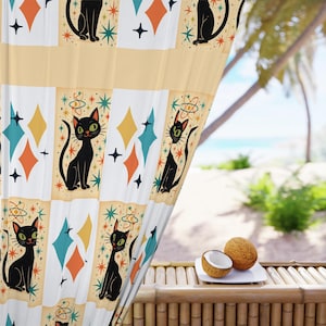 May include: Cream-colored curtain with a repeating pattern of black cat illustrations, diamonds, and starbursts. The cats have green eyes and are in various poses. The diamonds are in shades of orange, teal, and yellow. The curtain is near a tropical beach scene.
