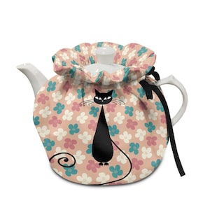 May include: A white ceramic teapot with a floral patterned cosy. The cosy features a black cat design and is decorated with pink, blue, and white flowers on a peach background. A black ribbon is tied to the handle.